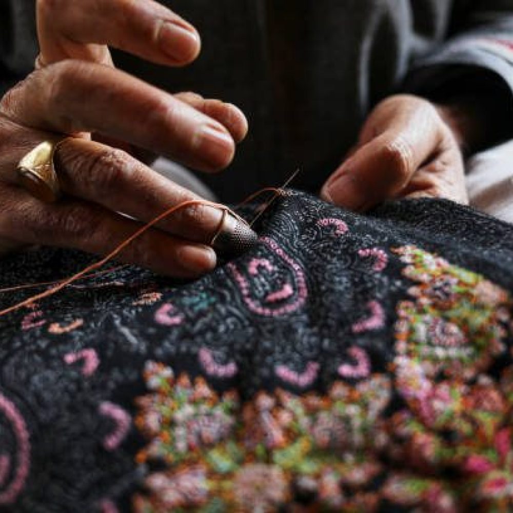 Creating art with every stitch - a master artisan delicately sewing intricate designs onto a Kashmiri shawl, transforming soft wool into a timeless masterpiece.